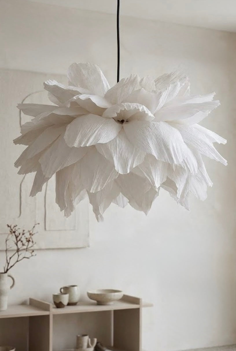 Hvit blomsterlampe i kreppapir over hylle i lys stue